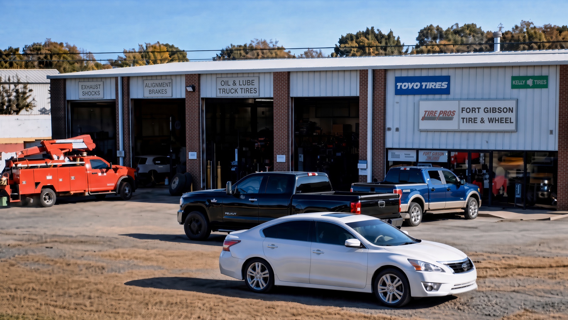 Metal shop building with open bays, stacked tires, and pickup trucks at late afternoon